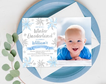 May include: A blue and silver snowflake themed invitation for a first birthday party. The invitation reads "Join us for a Winter Onederland to celebrate William's 1st Birthday". The invitation includes the date, time, address, and RSVP information. A photo of a baby boy is on the right side of the invitation.