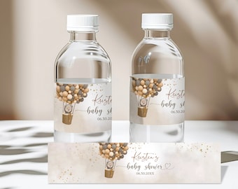 Pode incluir: Etiquetas para garrafas de água com um tema de balão de ar quente em tons de marrom, bege e cinza. O balão está cheio de pequenos balões e tem um pequeno urso na cesta. A etiqueta diz "Kristen's baby shower 06.30.20".