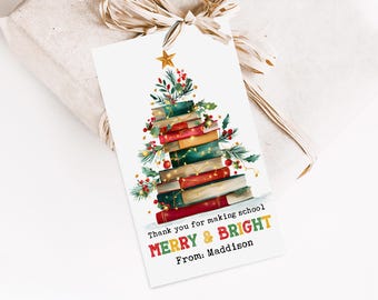 May include: A white gift tag featuring a Christmas tree design constructed from books. The tag includes the text "Thank you for making school MERRY & BRIGHT From: Maddison". The tag is attached to a wrapped gift with a beige ribbon.