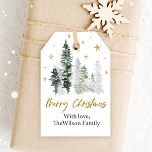 May include: White gift tag with a watercolor illustration of a forest scene with green and gray trees and gold stars. The text "Merry Christmas" and "With love, The Wilson Family" is printed in gold on the tag.