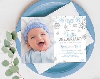 May include: A white invitation with a blue and silver snowflake design. The invitation is for a Winter Wonderland themed first birthday party for a baby named Liam. The invitation includes the date, time, location, and RSVP information.