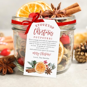 May include: A glass jar filled with stovetop Christmas potpourri ingredients, including dried orange slices, cinnamon sticks, and star anise. A red ribbon and a tag with instructions and the words "Merry Christmas" are attached.