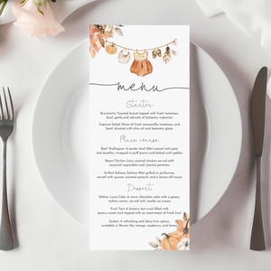 May include: A menu card with a fall theme, featuring a watercolor illustration of a baby outfit and pumpkins. The menu is on a white plate with a fork and knife. The menu includes starters, main courses, and desserts.