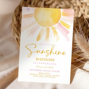 Può includere: Un biglietto d'invito bianco con un disegno di sole ad acquerello giallo, arancione e rosa. Il testo "Our Little Sunshine" è in oro, con i dettagli di una festa di primo compleanno, tra cui data, ora e luogo.
