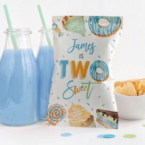 May include: A white favor bag with a blue and yellow design featuring donuts, ice cream cones, and cupcakes. The bag has the text "James is Two Sweet" printed on it.