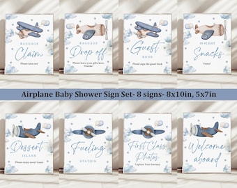 May include: Set of eight blue and white airplane themed baby shower signs. The signs feature illustrations of airplanes with clouds and stars. The signs have text that reads "Baggage Claim", "Baggage Drop Off", "Guest Book", "In-Flight Snacks", "Dessert Island", "Fueling Station", "First Class Photos", and "Welcome Aboard".