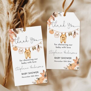 Puede incluir: Dos etiquetas blancas de agradecimiento para baby shower con cinta marrón. Las etiquetas tienen un diseño de acuarela con calabazas, hojas y ropa de bebé. El texto dice "thank you", "for showering our baby with love" y "BABY SHOWER November 10th 20xx".