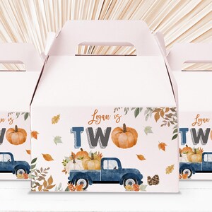 Può includere: Tre scatole portaconfetti a tema autunnale. Le scatole sono decorate con un camioncino blu che trasporta zucche, foglie autunnali e il testo "Logan ha due anni".