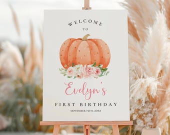 May include: A welcome sign for a first birthday celebration. The sign features a watercolor illustration of a pumpkin with polka dots, floral accents, and the name "Evelyn's" in pink script. The text "FIRST BIRTHDAY" and the date are also included.