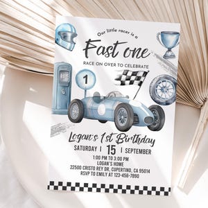 May include: A blue and white race car birthday invitation with a checkered flag, a trophy, a gas pump, and a racing helmet. The text reads "Our little racer is a Fast one Race on over to celebrate Logan's 1st Birthday Saturday | 15 | September 1:00 PM to 3:00 PM Logan's Home 22500 CRISTO REY DR, CUPERTINO, CA 95014 RSVP to EMILY at 123-456-7890"