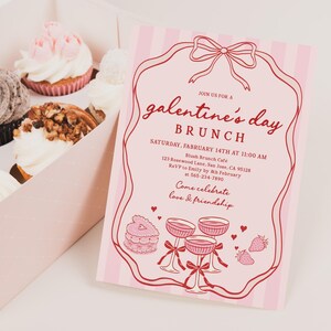 May include: A box of cupcakes with various toppings, including a chocolate cookie, nuts, and pink frosting, next to a pink Galentine's Day brunch invitation with red text and illustrations. The invitation includes the date, time, and location.