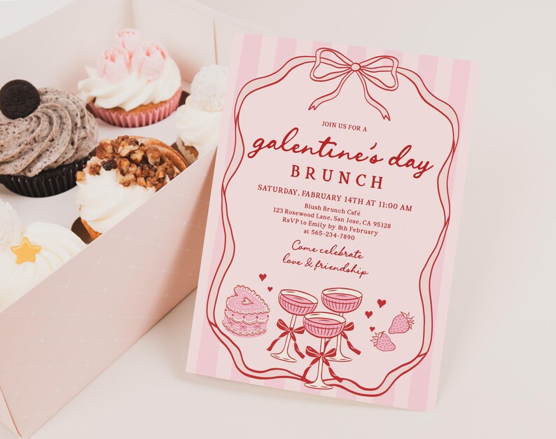 May include: A box of cupcakes with various toppings, including a chocolate cookie, nuts, and pink frosting, next to a pink Galentine's Day brunch invitation with red text and illustrations. The invitation includes the date, time, and location.