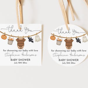 Może przedstawiać: Dwie zawieszki na baby shower z motywem Halloween. Każda zawieszka przedstawia sznur do wieszania ubrań z dynią, wiadrem, pajacykiem, nietoperzem i duchem. Tekst brzmi "Dziękuję" i "Baby Shower" z imieniem i datą.