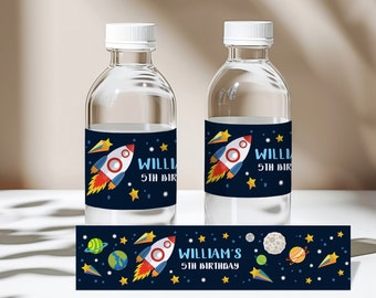 May include: Two clear plastic water bottles with blue and yellow space-themed labels. The labels feature a rocket ship, stars, and the text "William's 5th Birthday". A separate label with the same design is shown below the bottles.