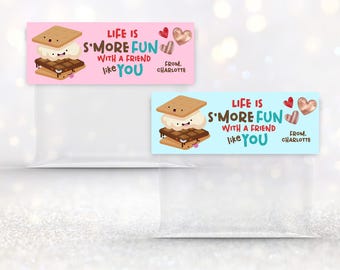 Könnte beinhalten: Zwei rechteckige Geschenkanhänger mit einer S'more-Grafik und dem Text "LIFE IS S'MORE FUN WITH A FRIEND LIKE YOU" und "FROM. CHARLOTTE". Einer ist rosa, der andere blau. Beide haben Herz- und herzförmige Akzente.