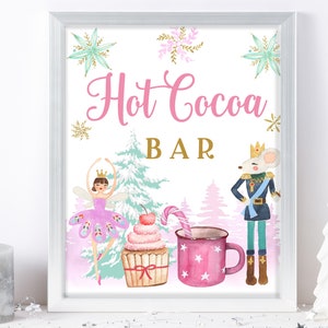 Puede incluir: Un cartel rosa y blanco con el texto "Hot Cocoa Bar" en letras rosas. El cartel presenta una ilustración de acuarela de una bailarina, un cascanueces, una magdalena y una taza de chocolate caliente.