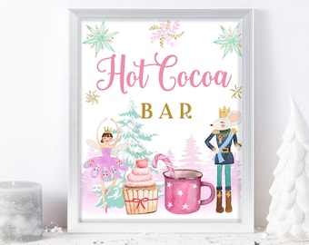 May include: A pink and white sign with the text "Hot Cocoa Bar" in pink lettering. The sign features a watercolor illustration of a ballerina, a nutcracker, a cupcake, and a mug of hot cocoa.