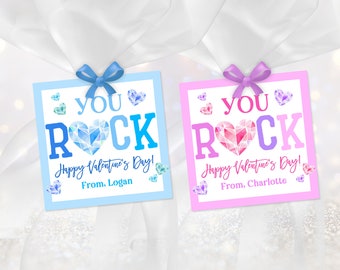 May include: Two Valentine's Day gift tags with a blue and pink background. The tags feature a large, colorful, geometric heart with the word "YOU" above it and "ROCK" below it. The text "Happy Valentine's Day!" is below the heart. The blue tag has the text "From, Logan" and the pink tag has the text "From, Charlotte".