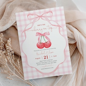May include: A rectangular baby shower invitation card featuring a light pink and white gingham background. The design includes a watercolour illustration of two red cherries tied with a pink ribbon, with the text: She's the cherry on top.