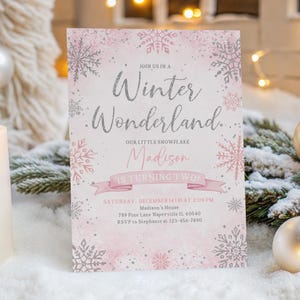 May include: A pink and silver Winter Wonderland invitation with snowflake accents. The invitation reads "Join us in a Winter Wonderland" and includes the name "Madison" and the phrase "is turning two".