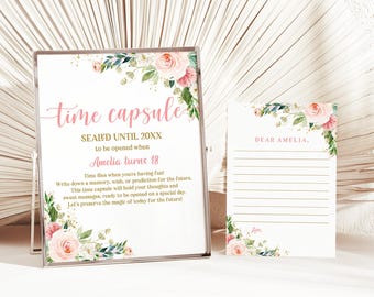 May include: A clear framed sign and a card with floral accents. The sign reads "time capsule" in pink script, with text below indicating it's for Amelia's 18th birthday. The card is addressed to "Dear Amelia" with lined space for writing.