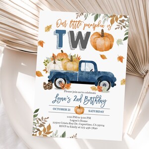 Può includere: Un camioncino blu con una cassone pieno di zucche, foglie e fogliame autunnale. Il camioncino sta guidando su uno sfondo bianco con il testo "Our little pumpkin is TWO" e "Logan's 2nd Birthday" in un font blu e grigio. L'invito include anche la data, l'ora e il luogo della festa.