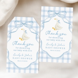 May include: Two baby shower thank you tags. The tags feature a blue gingham pattern and a watercolour illustration of a white goose with a blue bow. The text reads "Thank you for showering our baby with love".