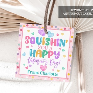 May include: A square Valentine's Day gift tag with a pink polka dot border and a brown string. The tag reads "Squishin' You a Happy Valentine's Day!" in colorful letters, with "From: Charlotte" at the bottom. The text "IT WON'T FIT ON ANY PRE-CUT LABEL PAPER" is at the top.