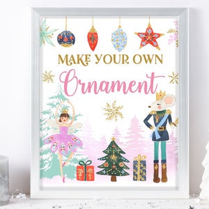 以下が含まれることがあります： 白い背景にピンク、ゴールド、ブルーの文字で「あなただけのオーナメントを作ろう」と書かれた印刷可能なサイン。サインには、バレリーナ、ナッツクラッカー、クリスマスツリーの幻想的なイラストが描かれています。