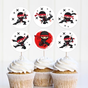 Puede incluir: Seis toppers redondos para cupcakes con un ninja de dibujos animados en negro y rojo con una cinta roja y estrellas ninja. Los toppers están sobre un fondo blanco con estrellas negras.