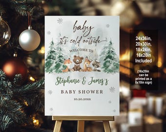 May include: A white sign with a winter woodland theme for a baby shower. The sign says "baby it's cold outside" and "Welcome to Stephanie & James's Baby Shower". The sign is decorated with snowflakes, pine trees, and woodland animals including a fox, a bear, a deer, and a raccoon. The sign is available in multiple sizes, including 24x36 inches, 20x30 inches, 18x24 inches, and 16x20 inches.