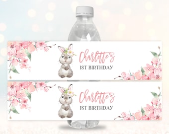 May include: Water bottle label with a pink floral design and a bunny illustration. The label says "Charlotte's 1st Birthday".