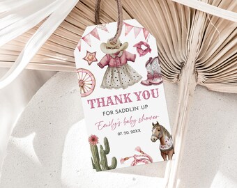 May include: A baby shower gift tag with a watercolor design. The tag features a pink and white cowboy theme with a cowboy hat, boots, and a dress. The text reads "THANK YOU FOR SADDLIN' UP" and "Emily's baby shower".