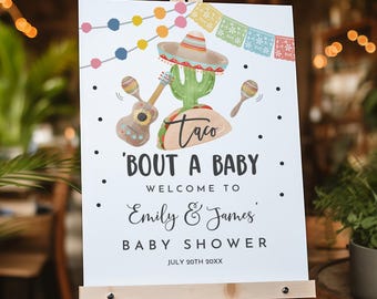 May include: A white rectangular sign on a wooden easel featuring a colorful illustration of a cactus wearing a sombrero, a guitar, and maracas. The text reads: Taco 'bout a baby, Welcome to Emily & James' Baby Shower, July 20th 20xx.