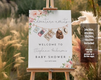 May include: A white sign with pink flowers and a travel theme. The sign says "Adventure awaits" and "Welcome to Stephanie Anderson's Baby Shower" with the date "July 20th 20XX". The sign is on a wooden easel and is available in sizes 24x36 inches, 20x30 inches, 18x24 inches, and 16x20 inches. The 16x20 inch size can be printed as an 8x10 inch sign.