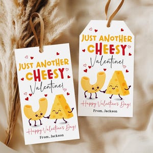 May include: Two white gift tags with brown string, featuring the text "Just Another Cheesy Valentine!" in orange and red. Cartoon macaroni and cheese characters hold hands. The tags read "Happy Valentine's Day!" and "From, Jackson."