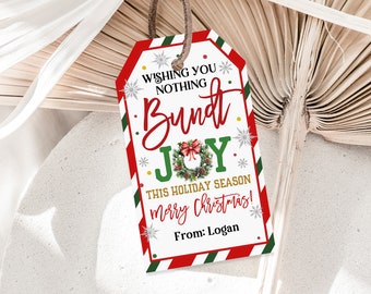 Pode incluir: Uma etiqueta de presente de Natal branca com listras vermelhas e verdes. A etiqueta apresenta uma coroa dourada e verde com um laço vermelho e as palavras "Wishing you nothing but joy this holiday season Merry Christmas! From: Logan".