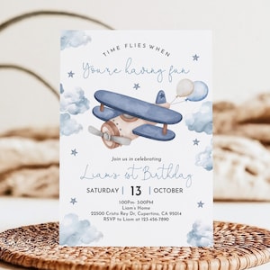 May include: A blue and white airplane with a brown propeller flies through the clouds. The text "TIME FLIES WHEN YOU'RE HAVING FUN" is at the top of the invitation. The invitation is for Liam's 1st Birthday party on Saturday, October 13th from 1:00 PM to 3:00 PM. The address and RSVP information are included.