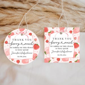 May include: Two paper gift tags, one circular and one square, featuring a pink strawberry pattern. The text reads: THANK YOU berry much for making our baby shower so berry special, Jennifer's baby shower, July 10th, 20xx. Each tag has a white string.