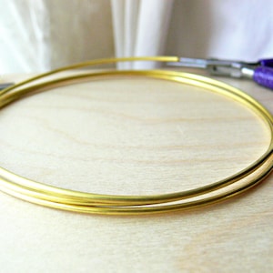 May include: Two gold-coloured metal hoops, one slightly larger than the other, are lying on a light wood surface.
