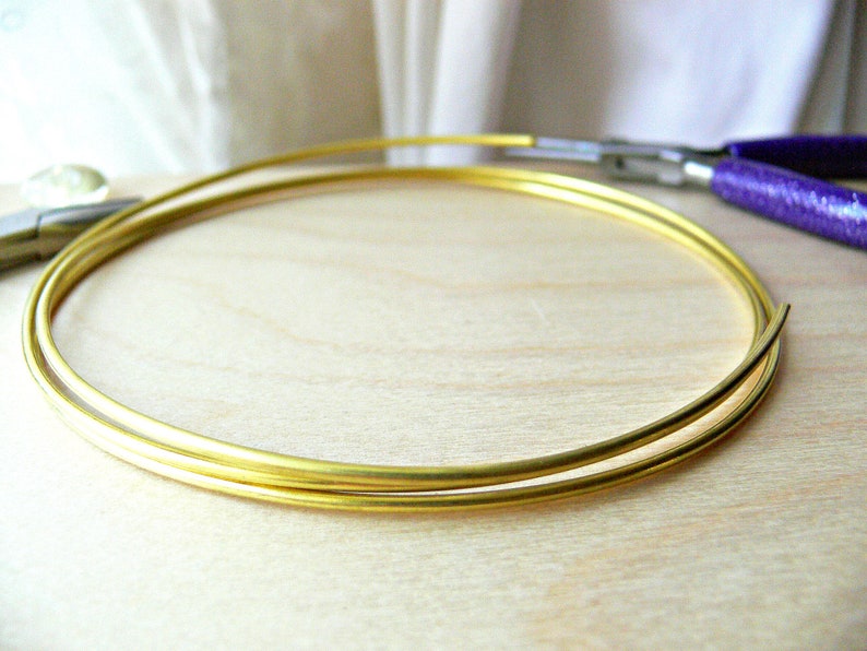May include: Two gold-coloured metal hoops, one slightly larger than the other, are lying on a light wood surface.