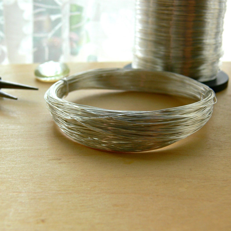 May include: A spool of silver wire, with a coil of the wire laid out on a wooden surface.
