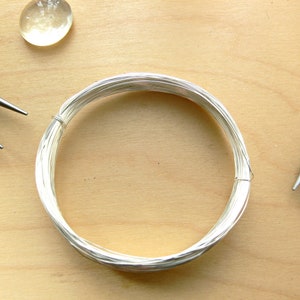 May include: A coil of silver wire on a wooden surface with two pairs of pliers.