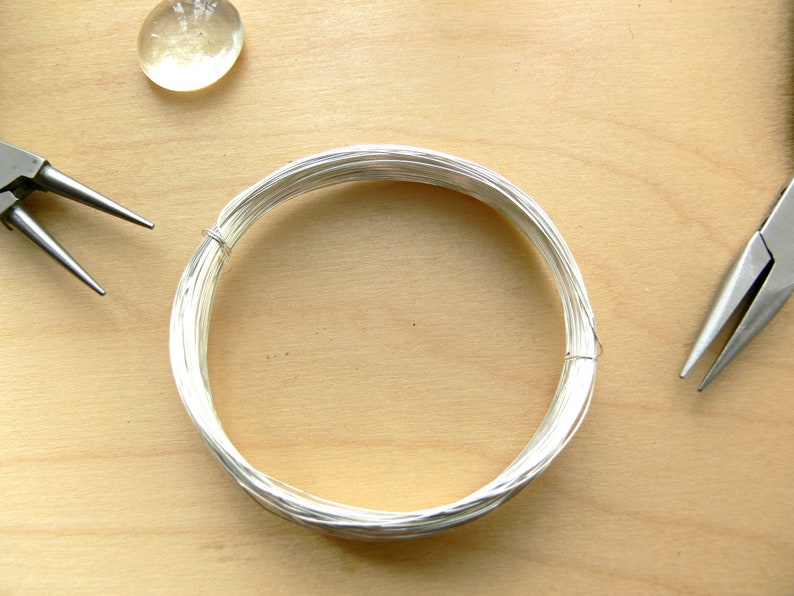 May include: A coil of silver wire on a wooden surface with two pairs of pliers.