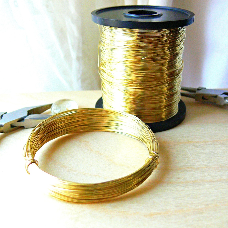 May include: A spool of gold-colored wire with a black plastic spool. A coil of the wire is lying on a wooden surface.