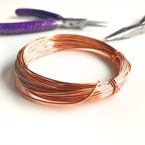 Peut inclure: Un rouleau de fil de cuivre, un matériau de bricolage courant, est présenté sur une surface blanche. Le fil est de couleur brun rougeâtre chaud et est enroulé étroitement.