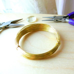 May include: A coil of gold-colored wire on a wooden surface. Two pairs of pliers are also visible in the image.