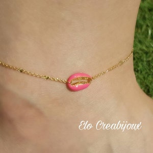 May include: A gold chain anklet with a pink seashell charm. The anklet is on a person's ankle.