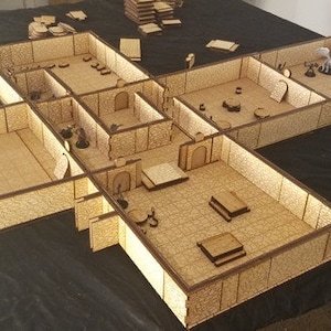 May include: A wooden dungeon set for tabletop role-playing games. The set includes multiple rooms and walls, with a brown finish. The set is assembled on a black surface.