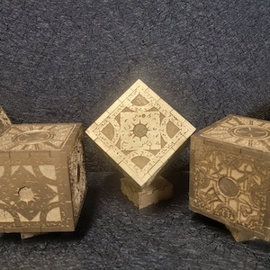 May include: Five wooden puzzle boxes with intricate designs and a gold finish. The boxes are arranged in a row on a dark gray surface.